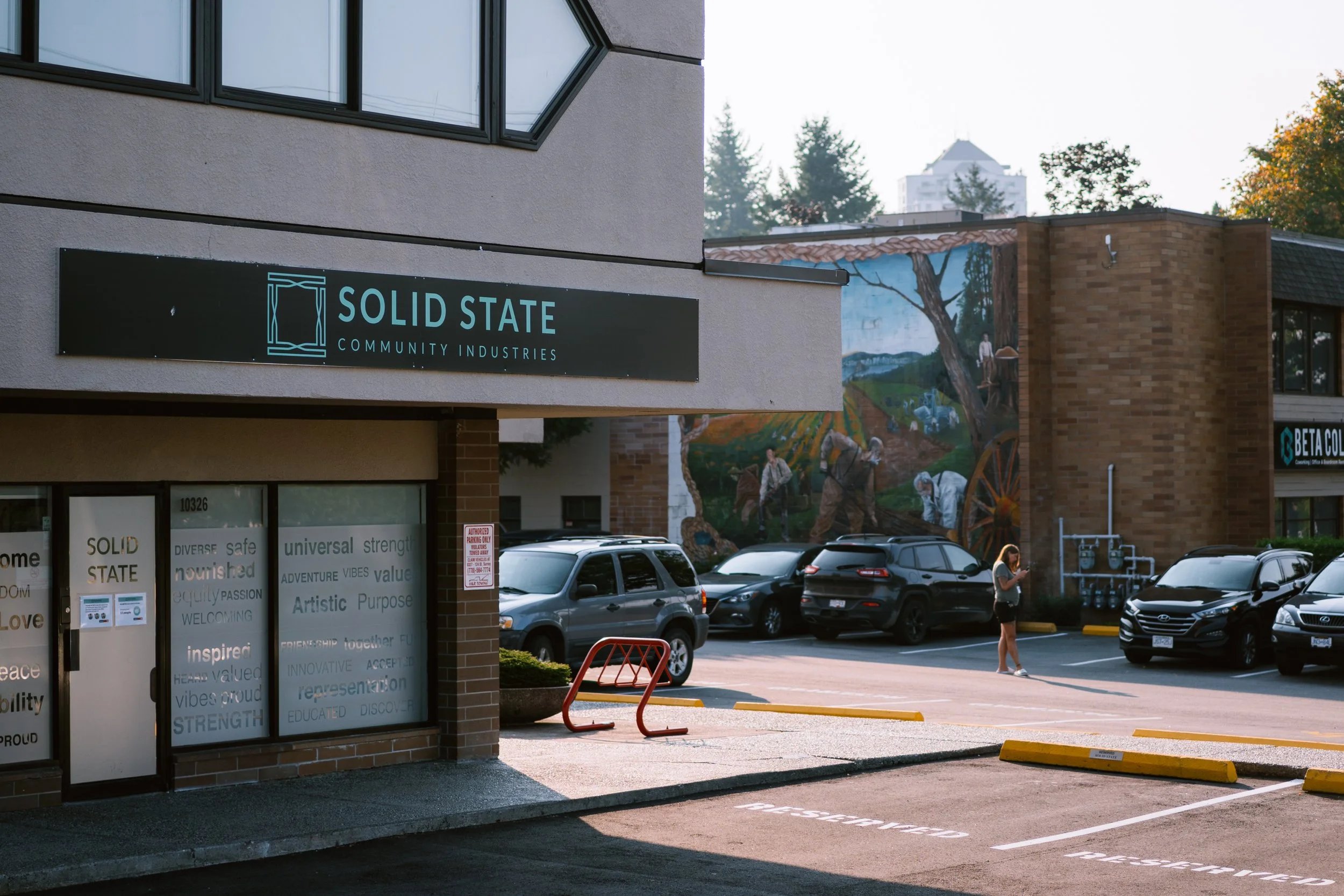 Commercial building with a “SOLID STATE COMMUNITY INDUSTRIES” sign, mural, and parked cars.